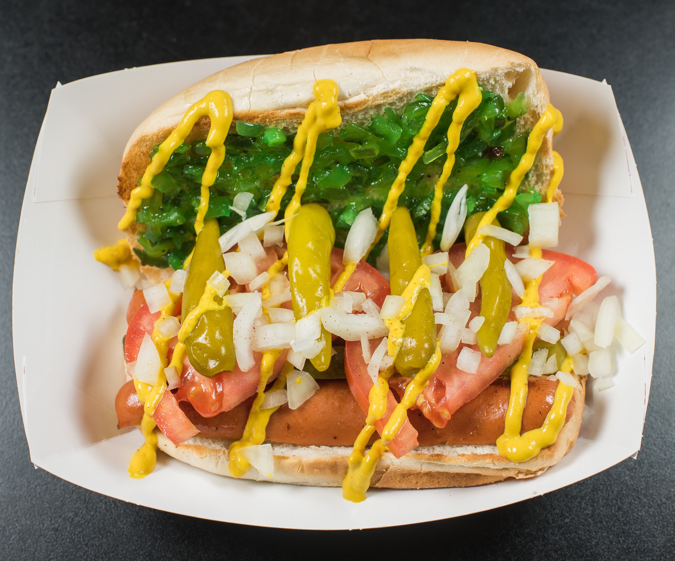 Pictured here:  Chicago Dog featuring Relish, Onions, Dill Pickle, Tomato, Sport Peppers, Mustard and Celery Salt. Vegetarian Option Available.